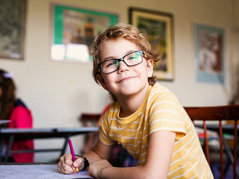 Boy with glasses smiling and taking notes in class