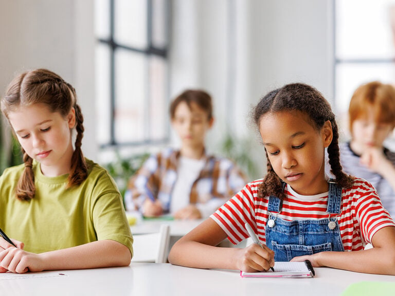 Two girls in class at their desks looking down writing