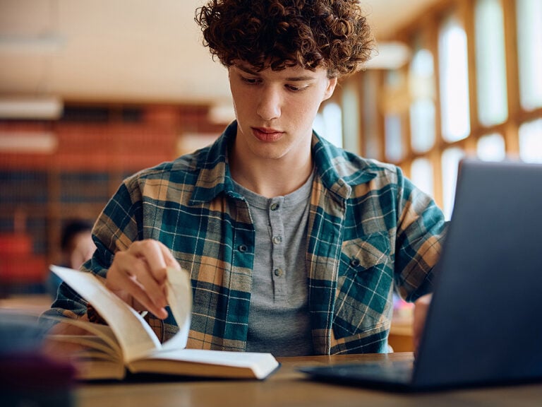 Male student reading book at school library