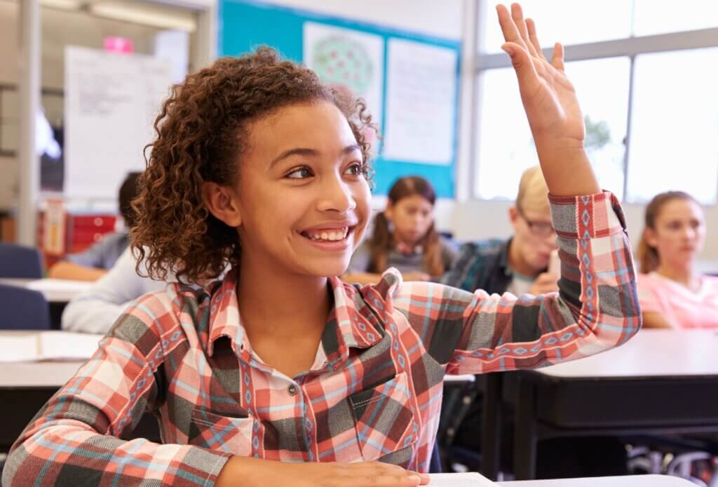 Schoolgirl at desk in elementary school raising her hand