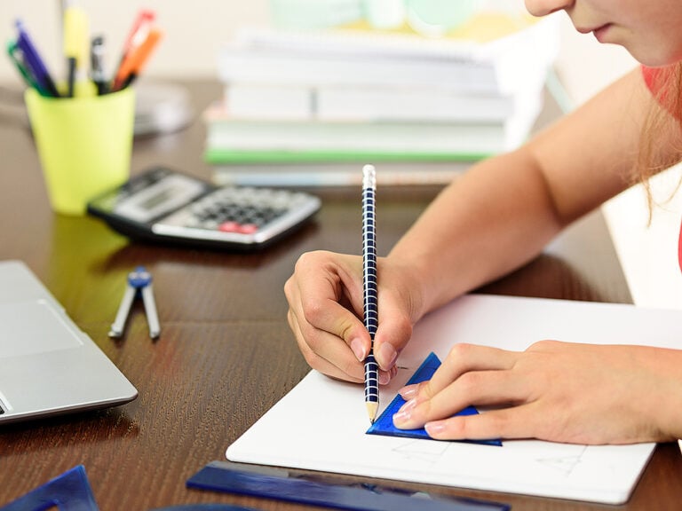 Girl doing a homework with math and geometry next to a laptop, calculator and books on her desk in her room