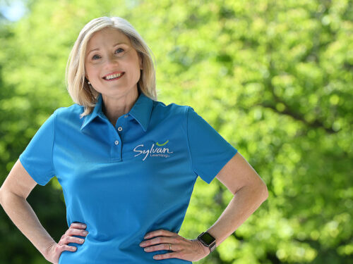 Portrait of blonde Sylvan tutor wearing blue Sylvan polo shirt outside in front of trees